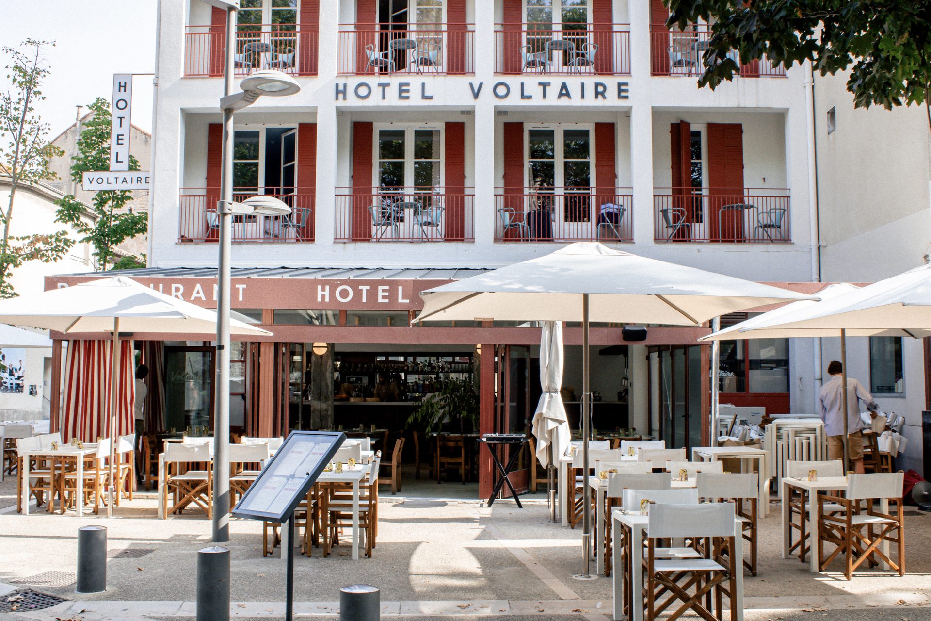 Terrasse de l'Hôtel Voltaire, tables blanches et parasols sur la place